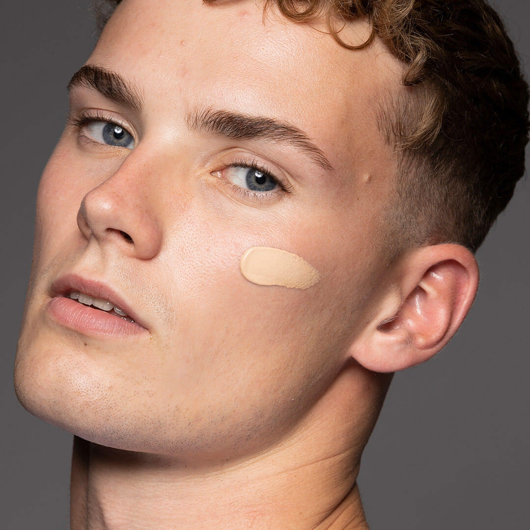Close-up of a person with concealer applied on their face against a neutral background
