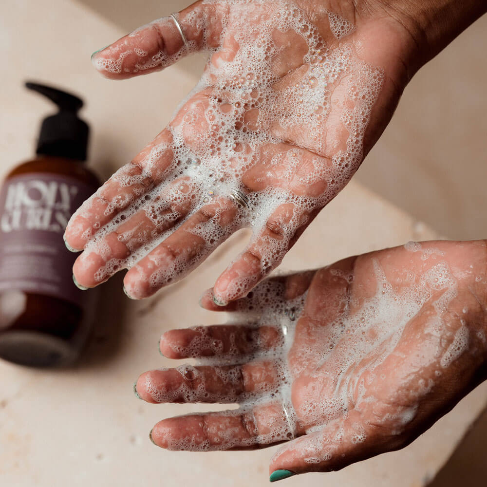 Foamy hands with a bottle of soap on a neutral background