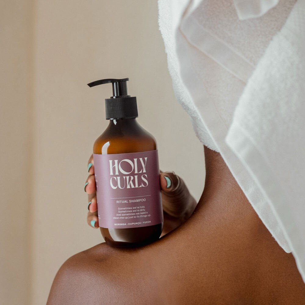 Person holding a bottle of 'Holy Curls' shampoo with a neutral background