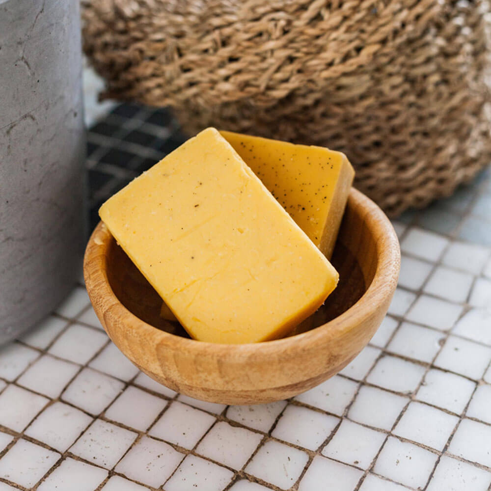 Two yellow soap bars in a wooden bowl on a tiled surface.