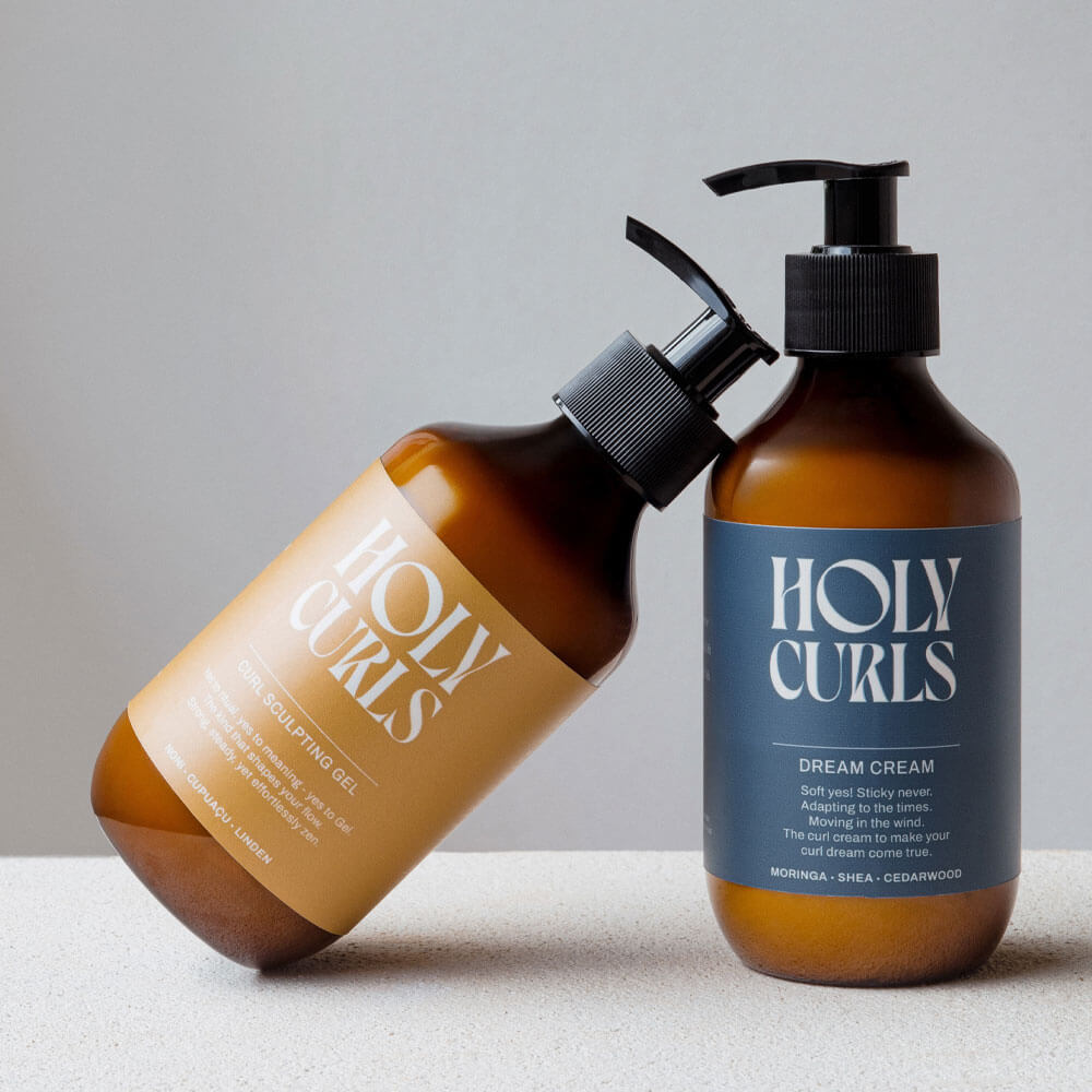 Two bottles of Holy Curls hair care products on a neutral background