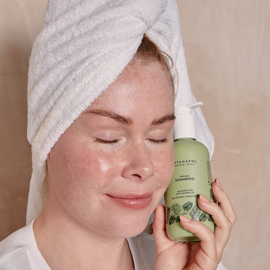 Person with a towel wrapped around their head holding a bottle of shampoo.