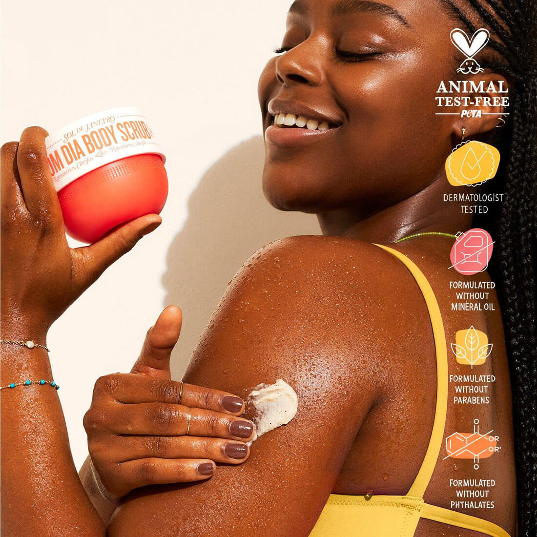 Woman applying a body scrub to her shoulder with product packaging and branding details.