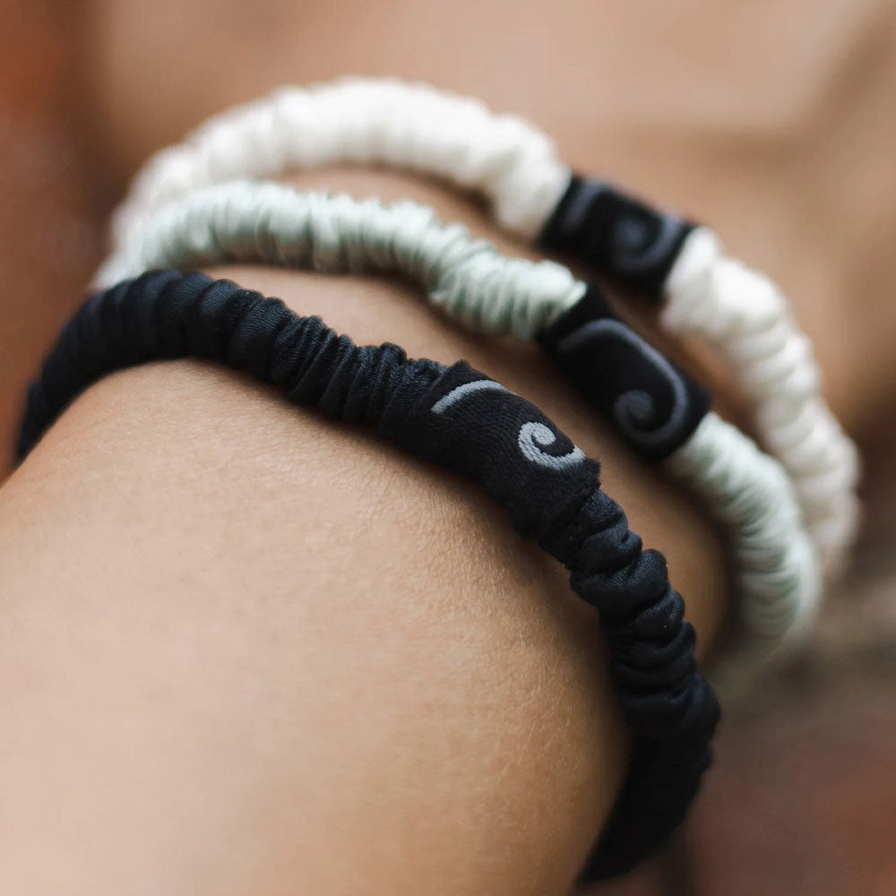 Two bracelets, one black and one white, on a wrist with a blurred background.