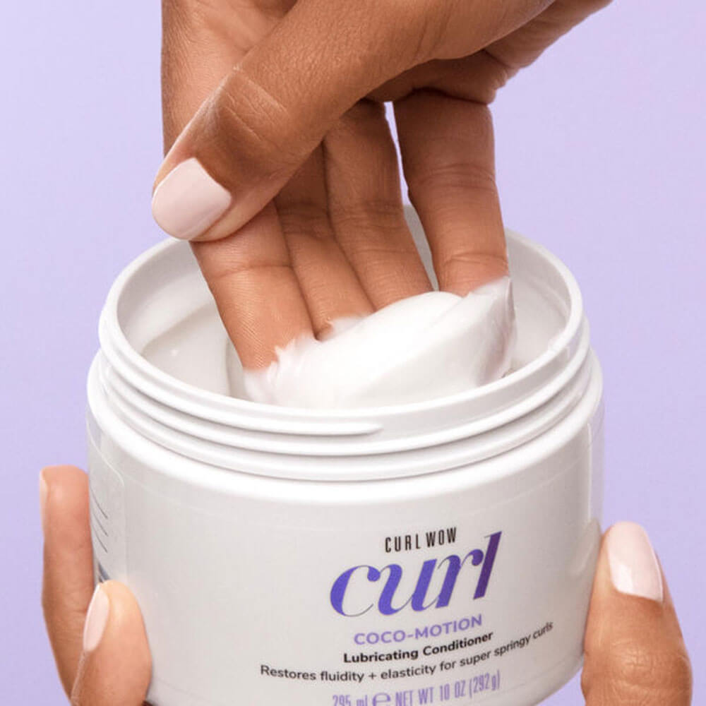 Hand holding a jar of Curl Wow Coco-Motion conditioner with a purple background