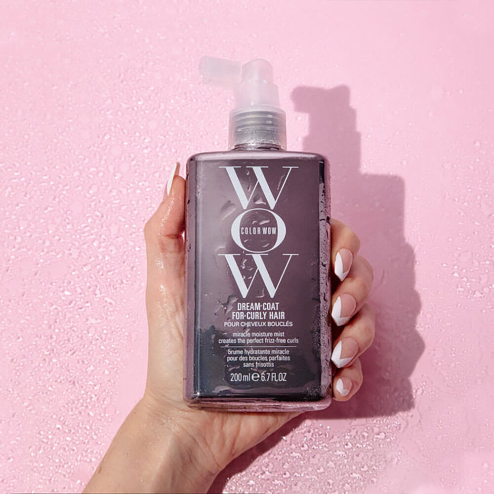 Hand holding a bottle of WOW Color Wet Dream Coat against a pink background