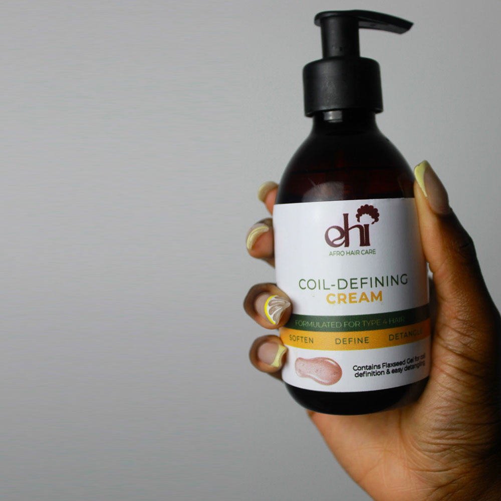 Hand holding a bottle of 'dhi' coil-defining cream against a gray background
