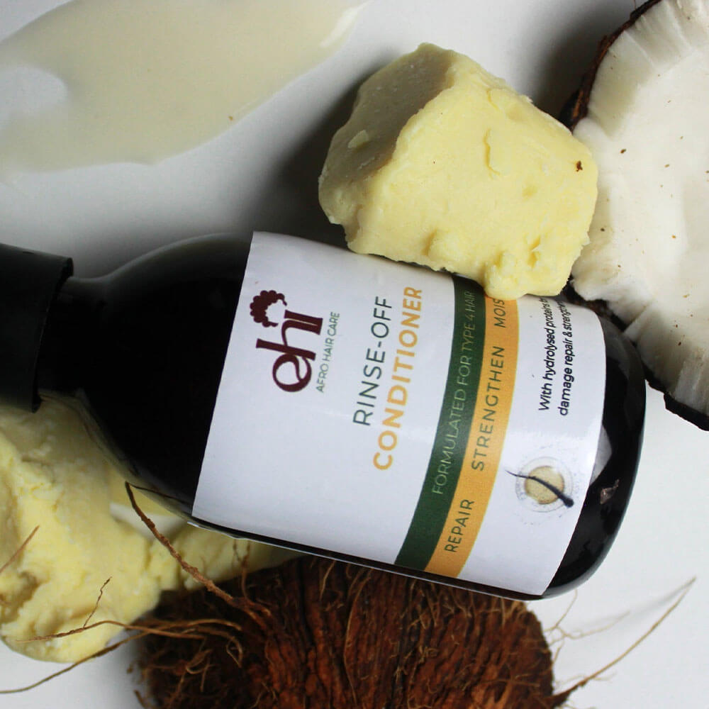 Bottle of 'eh!' rinse-off conditioner with soap bars and a coconut on a white background
