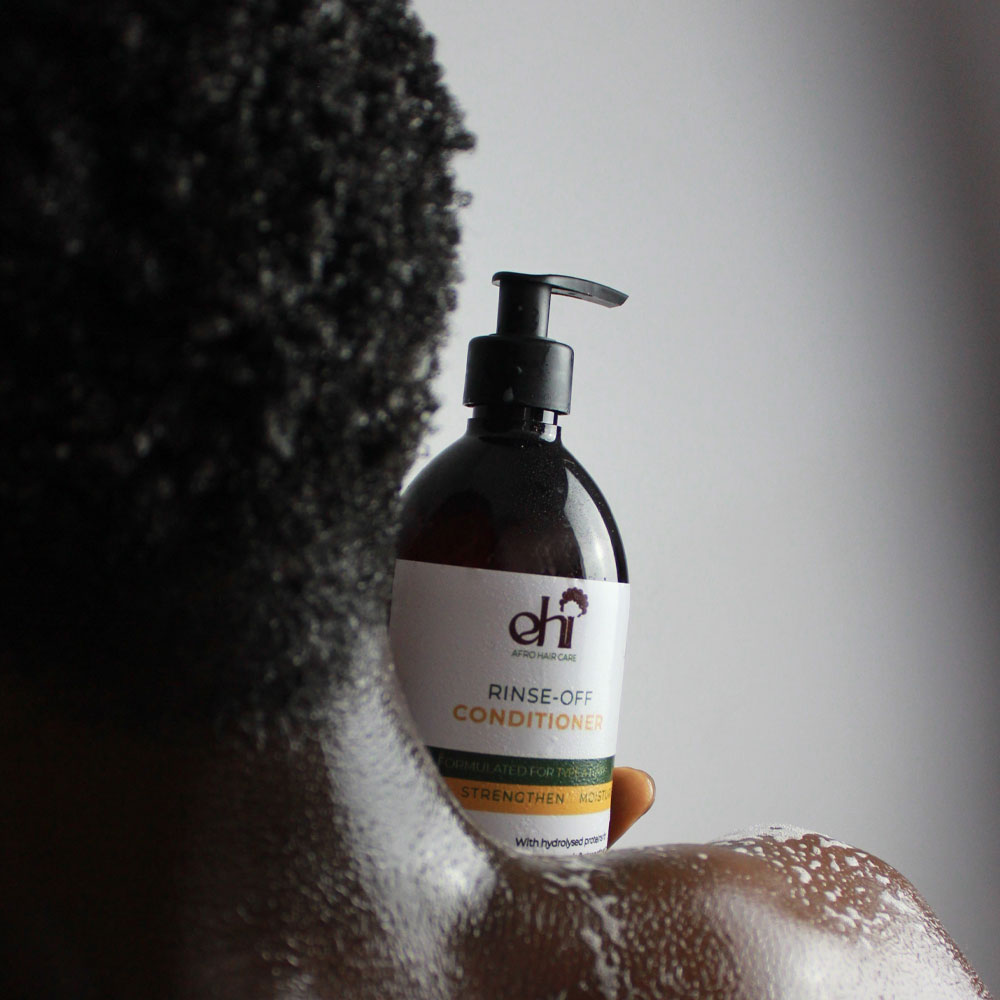 Bottle of Rinse-Off Conditioner held by a person with textured hair against a neutral background