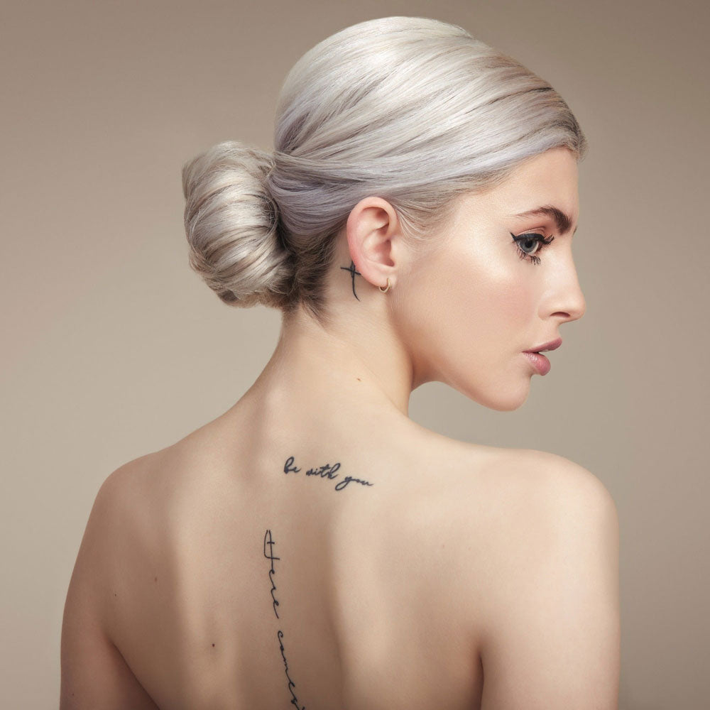 Woman with styled hair and tattoos on her neck and shoulder against a beige background