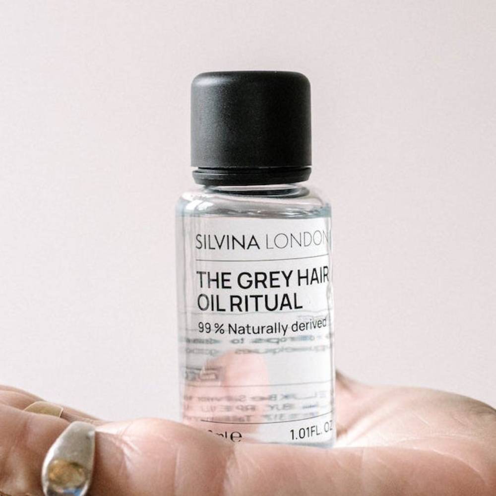 Bottle of 'The Grey Hair Oil Ritual' by Silvina London held in a hand with a light background.