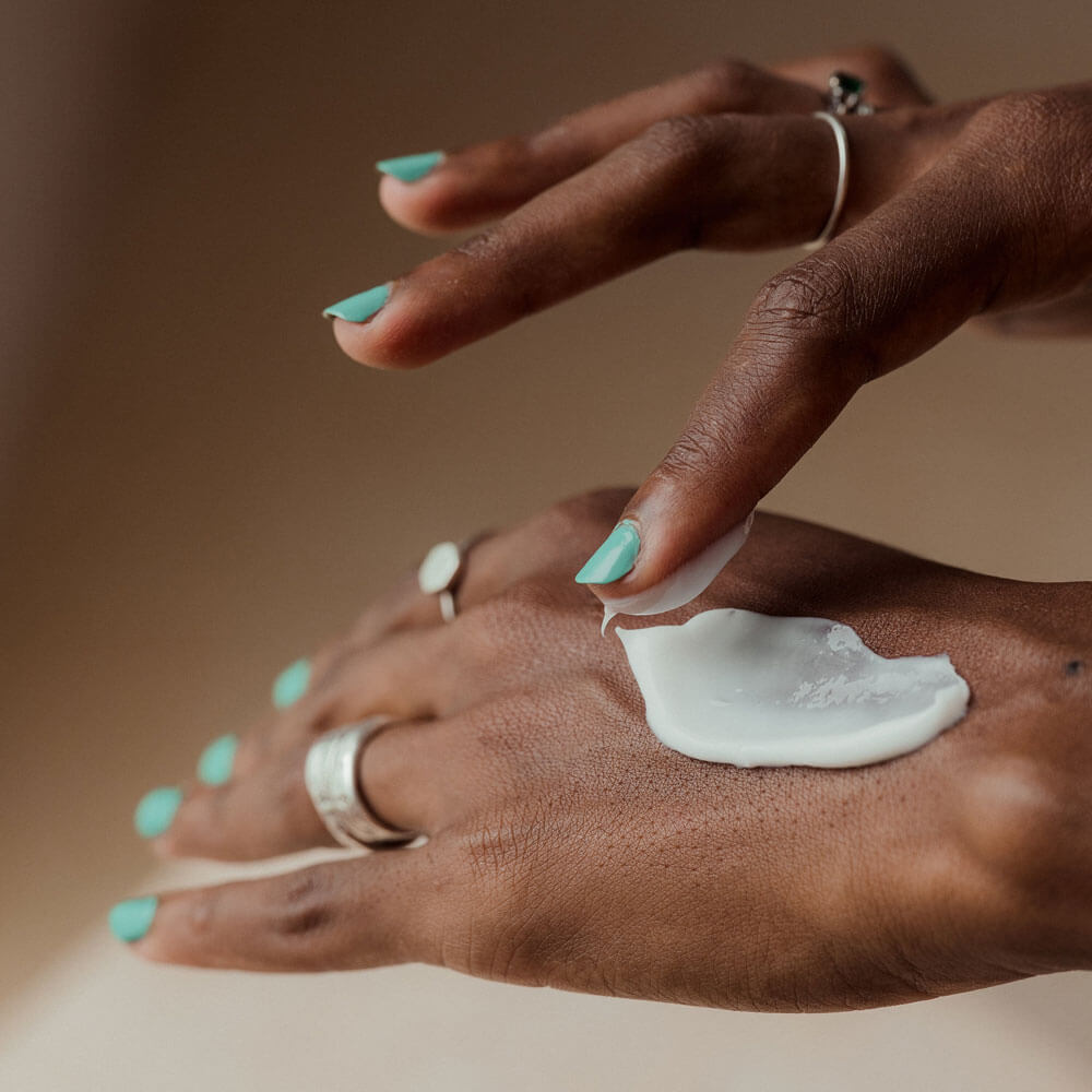 Hand applying cream to another hand with a neutral background