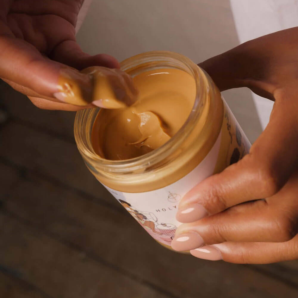 Person scooping peanut butter from a jar with a focus on the action.