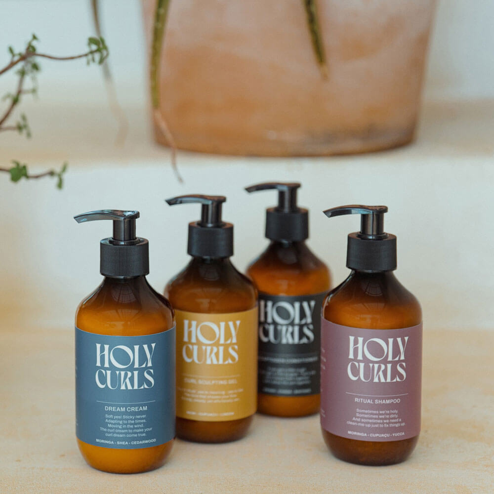 Four bottles of Holy Curls products on a neutral background