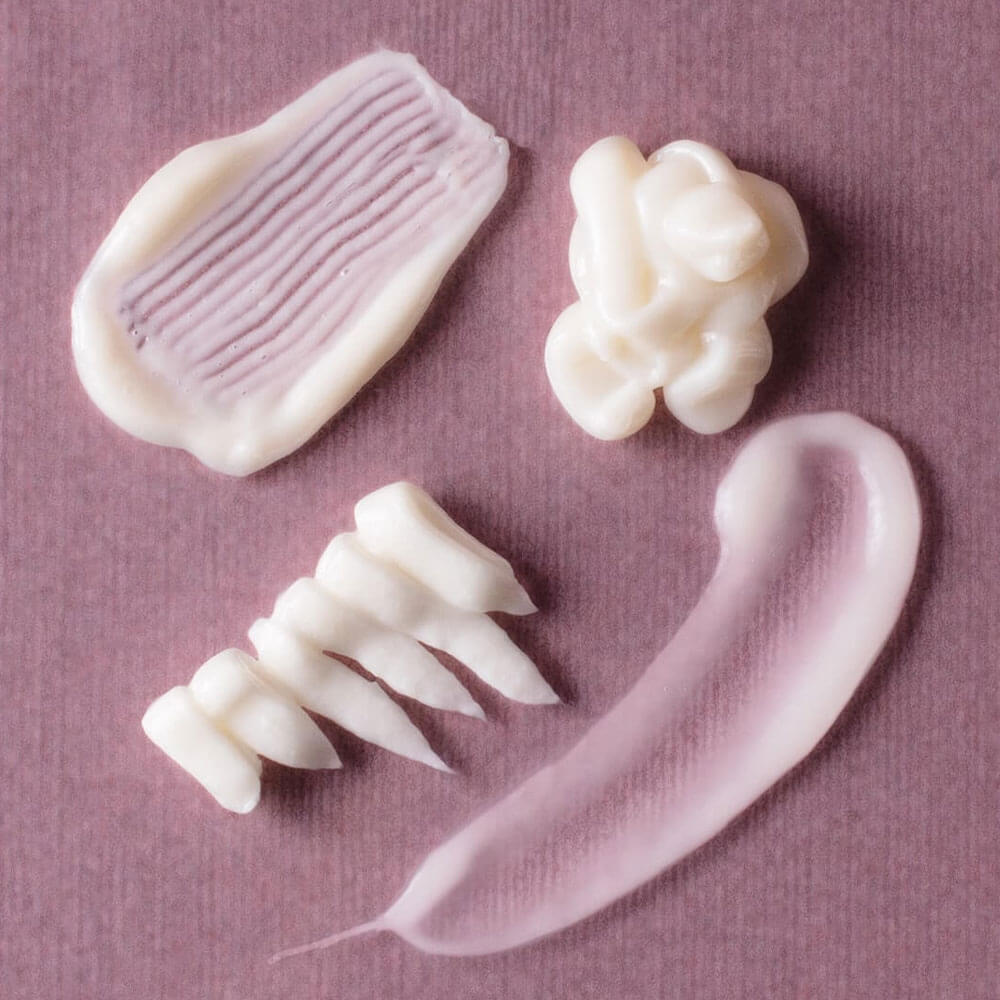 Five different textures of white cream on a pink background