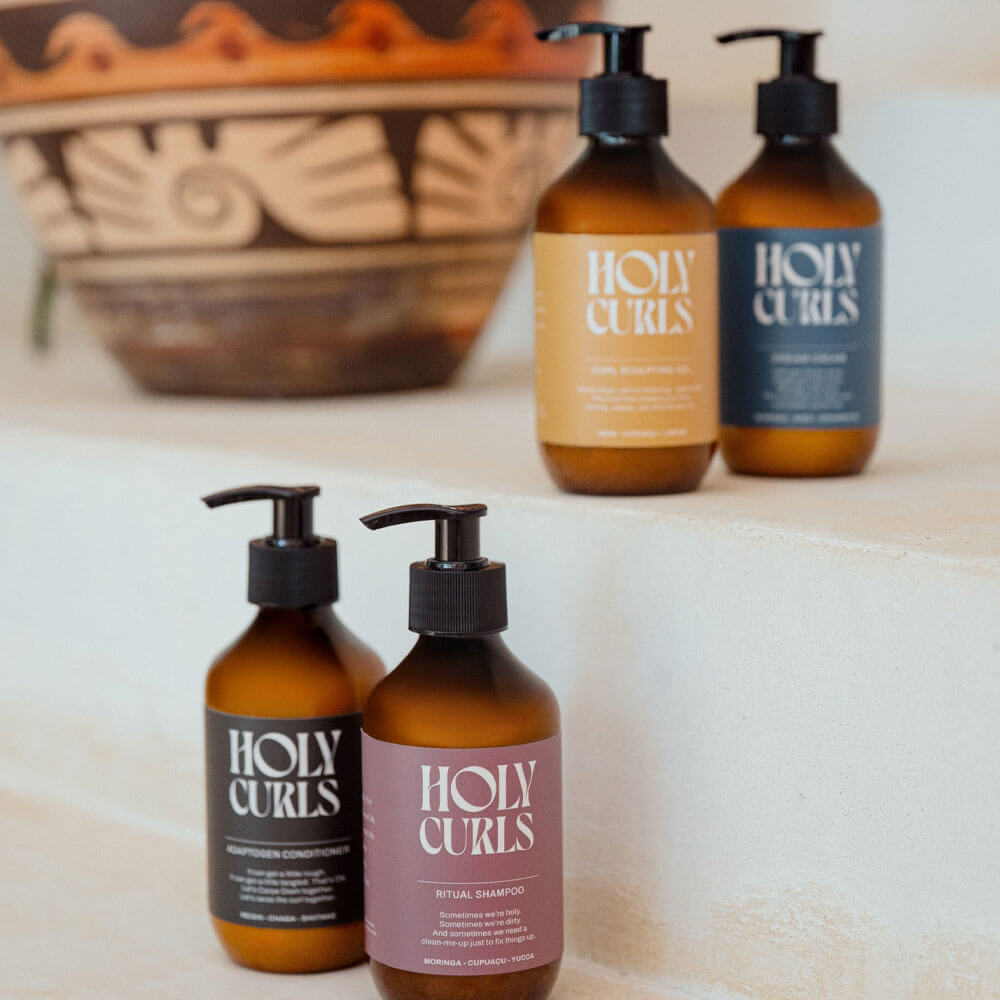 Holy Curls hair care products on a towel with a decorative bowl in the background