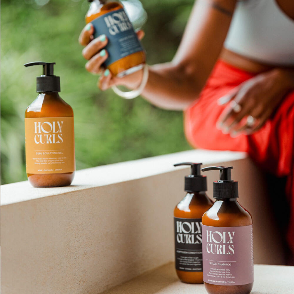 Bottles of Holy Curls hair care products on a ledge with a person in the background.