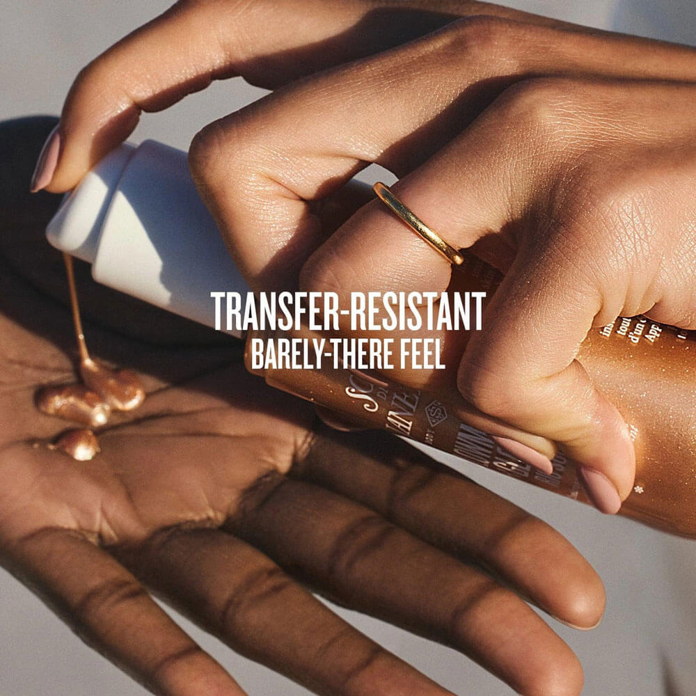 Hand applying a cosmetic product with text 'Transfer-Resistant Barely-There Feel' on a neutral background