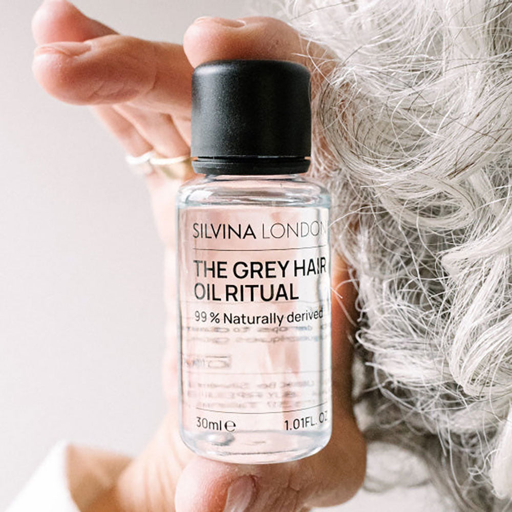 Bottle of Silvina London Grey Hair Oil Ritual held by a hand with white hair.