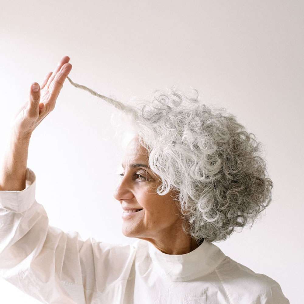 Woman with gray hair touching her hair against a white background