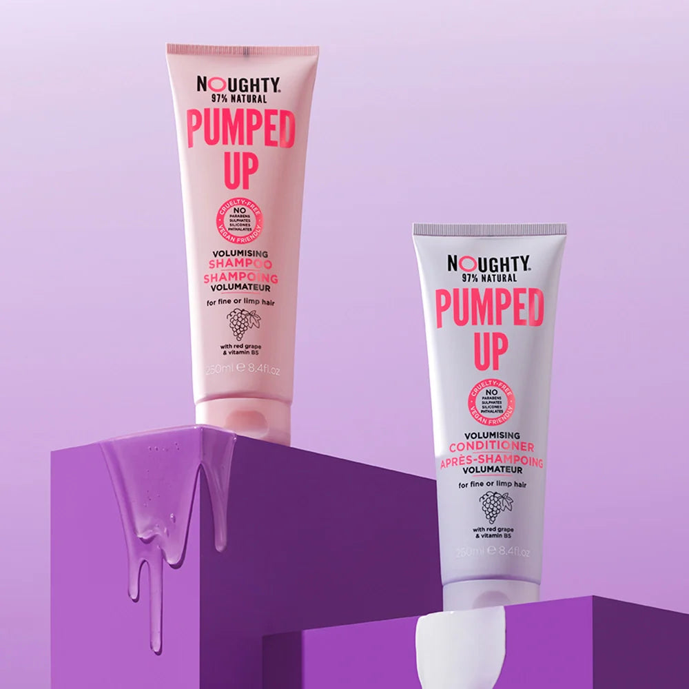 Two tubes of 'Noughty Pumped Up' shampoo and conditioner on a purple background