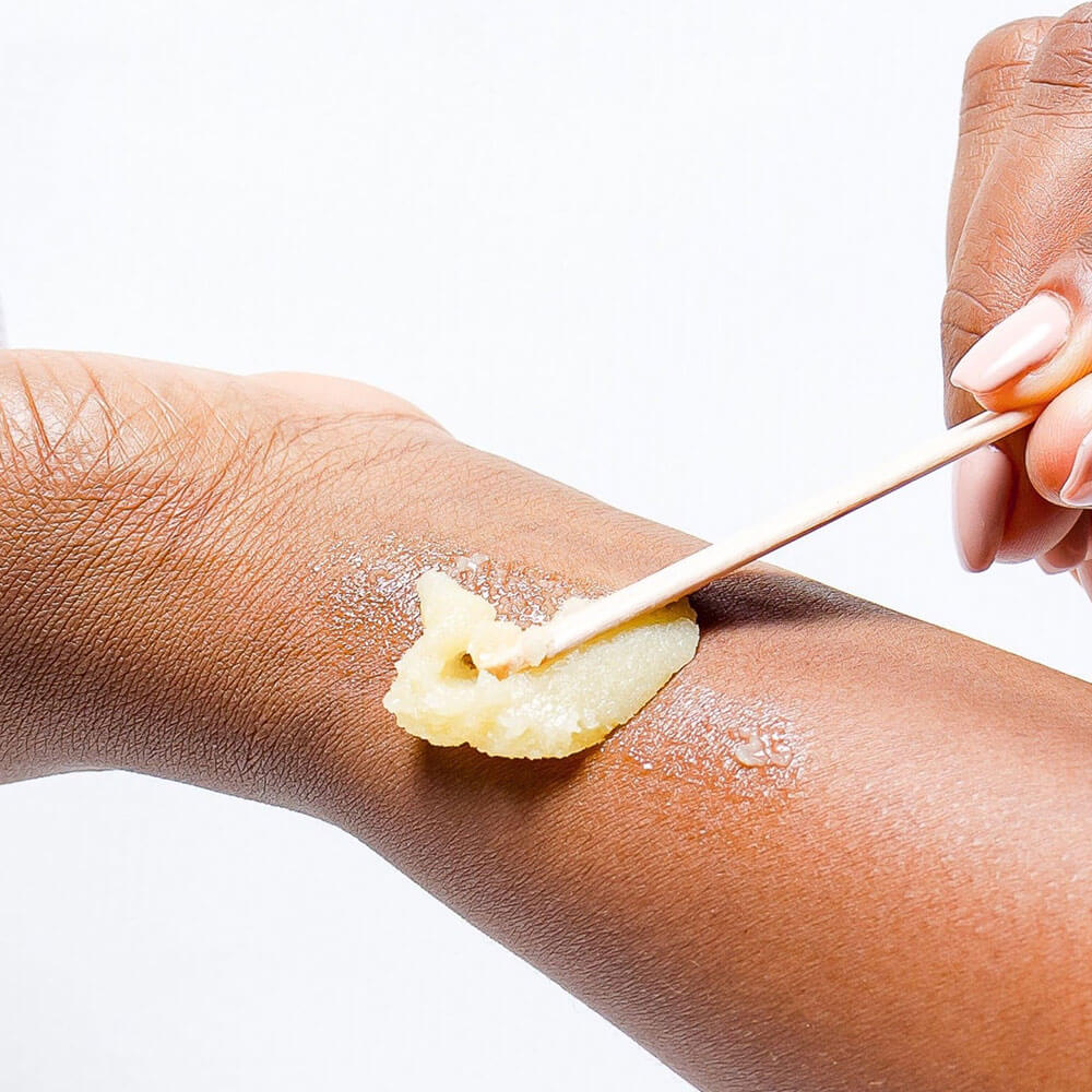 Person applying eczema  balm to their arm with a wooden stick on a white background