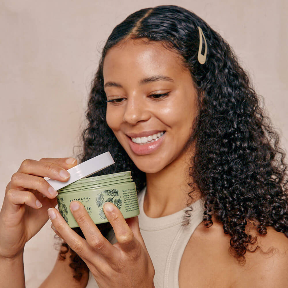 Woman holding a green jar with a white lid, smiling against a beige background