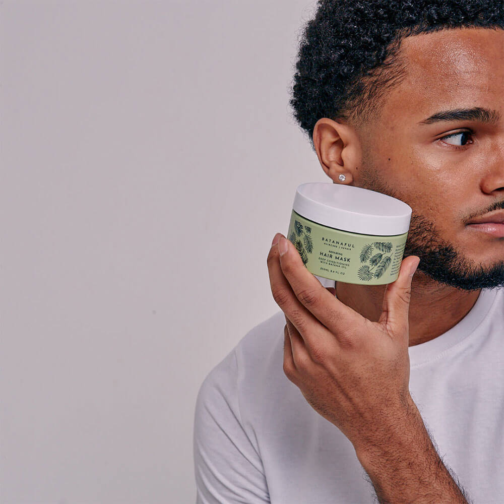 Man holding a hair wash product with a green label against a plain background