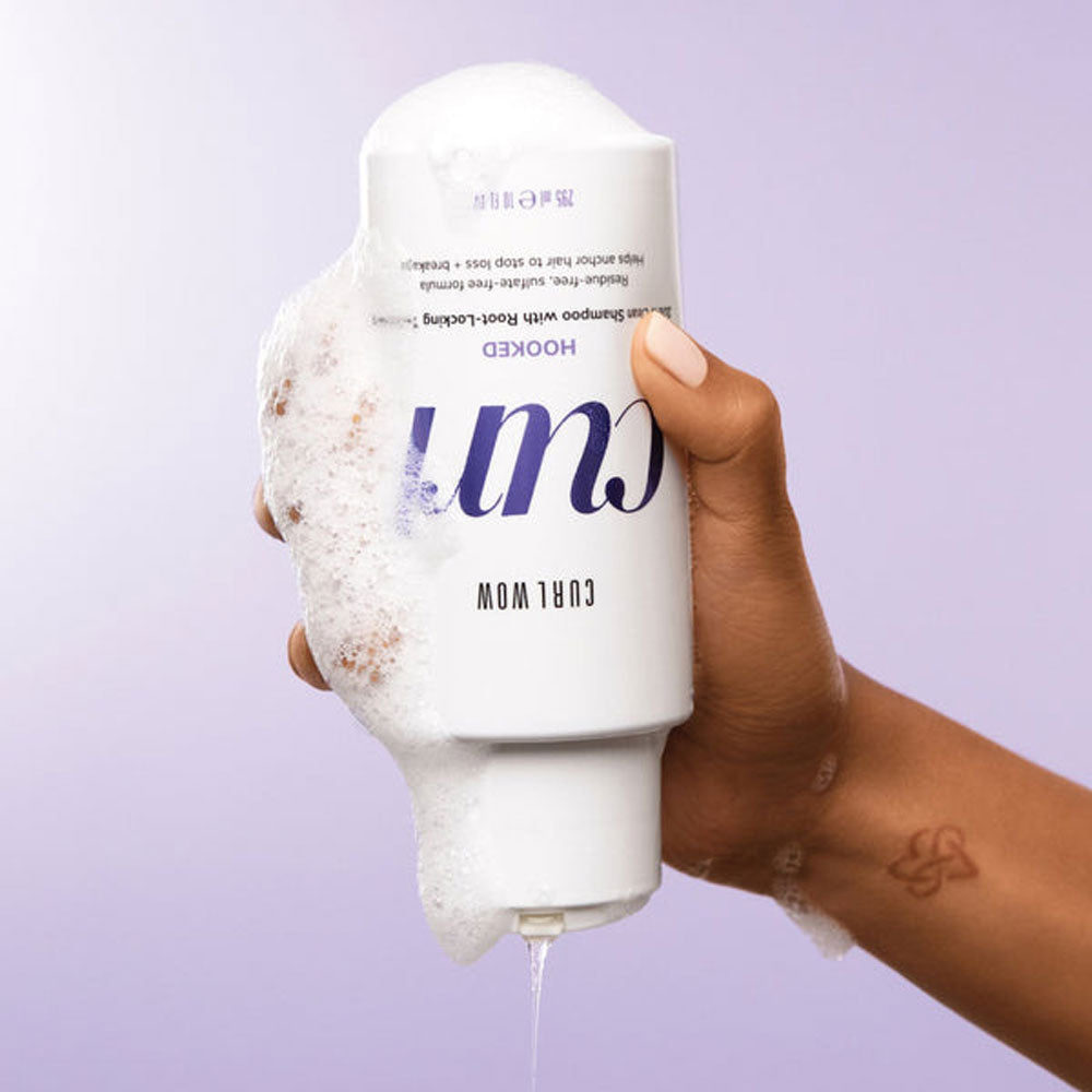 Hand holding a bottle of 'Curl' product with a purple background
