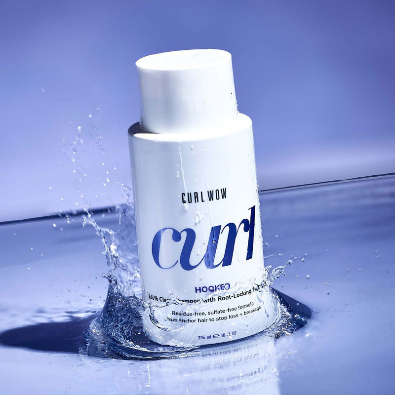 Bottle of Curl Wow hair product with water splash on a blue background