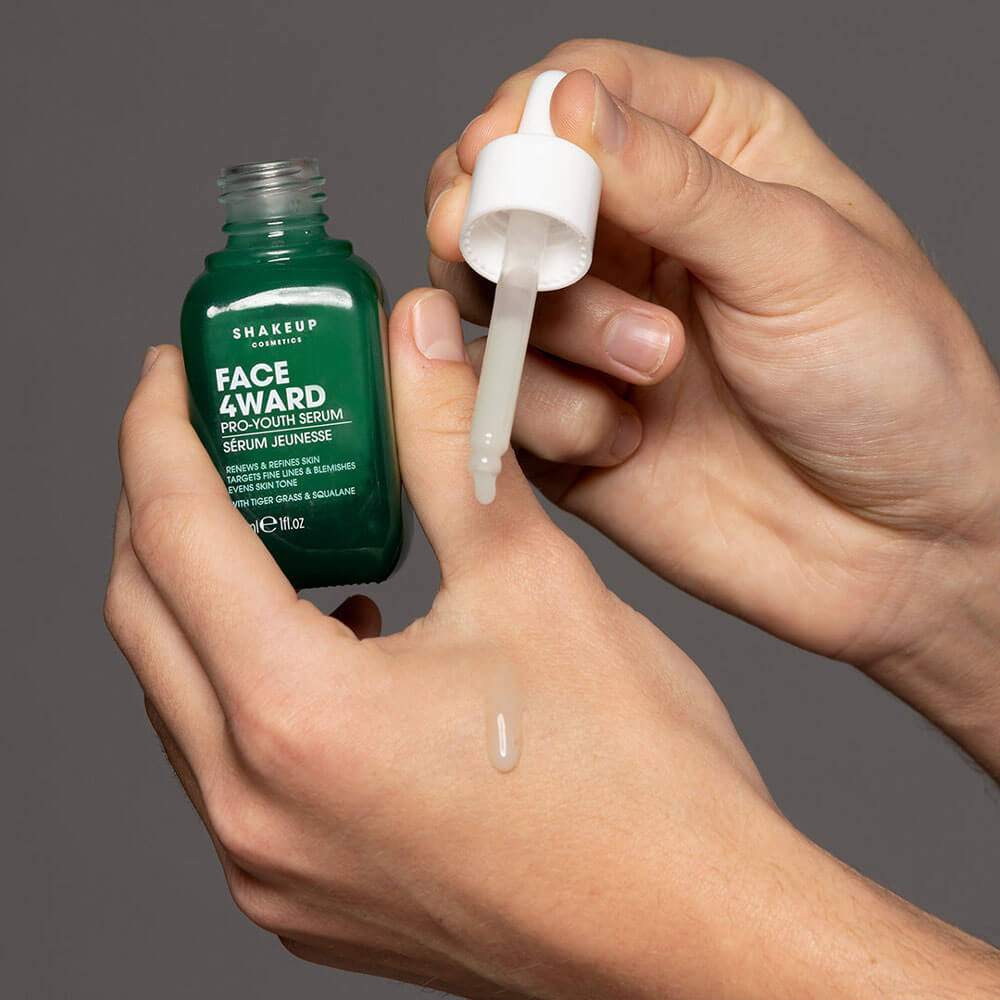 Person holding a green serum bottle and dropper with a gray background