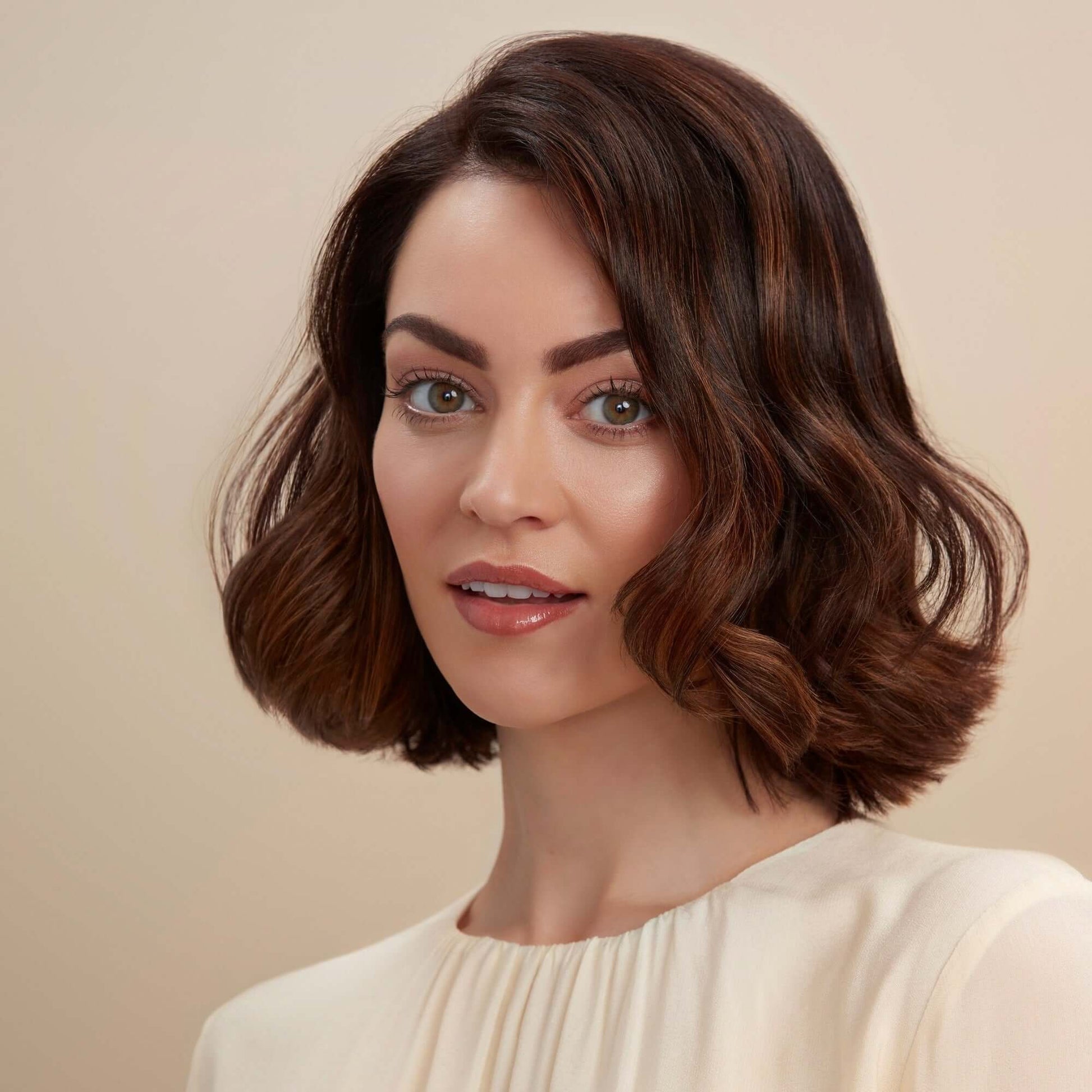 Woman with styled brown hair against a beige background