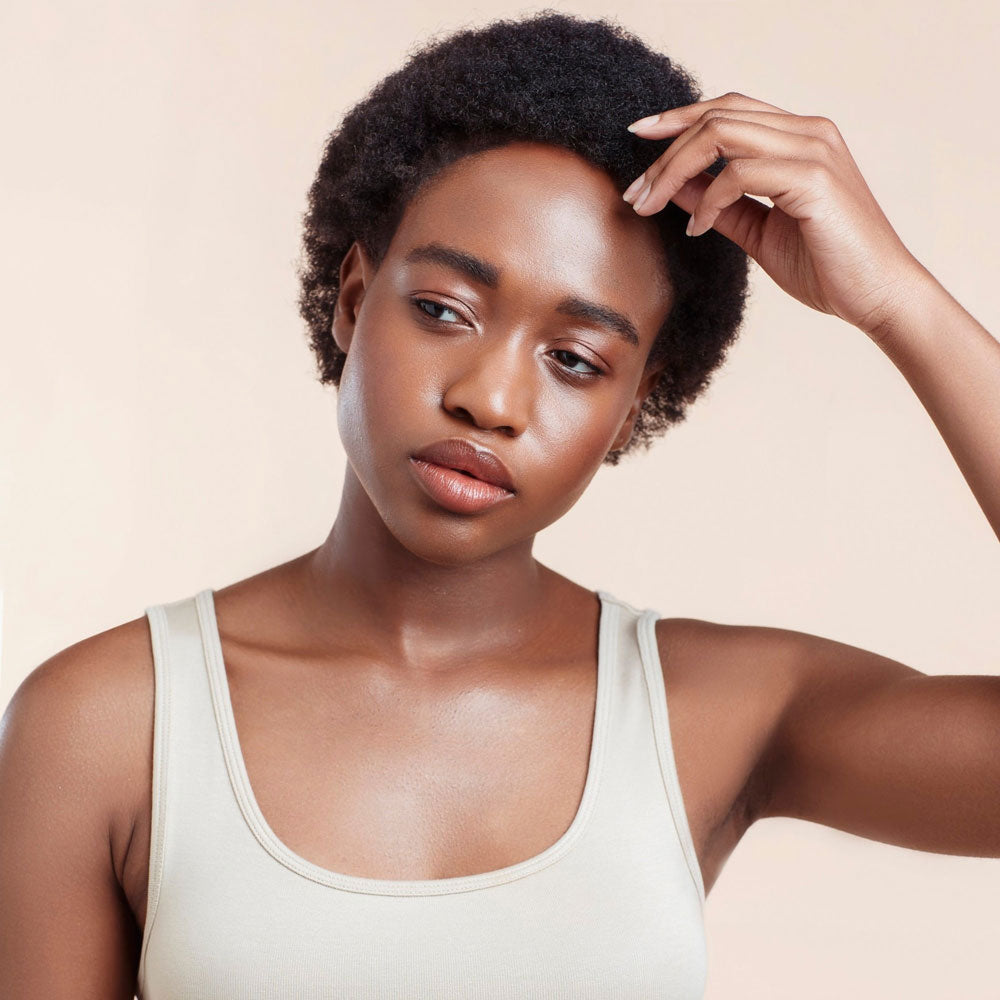 Woman with natural hair wearing a white tank top against a beige background