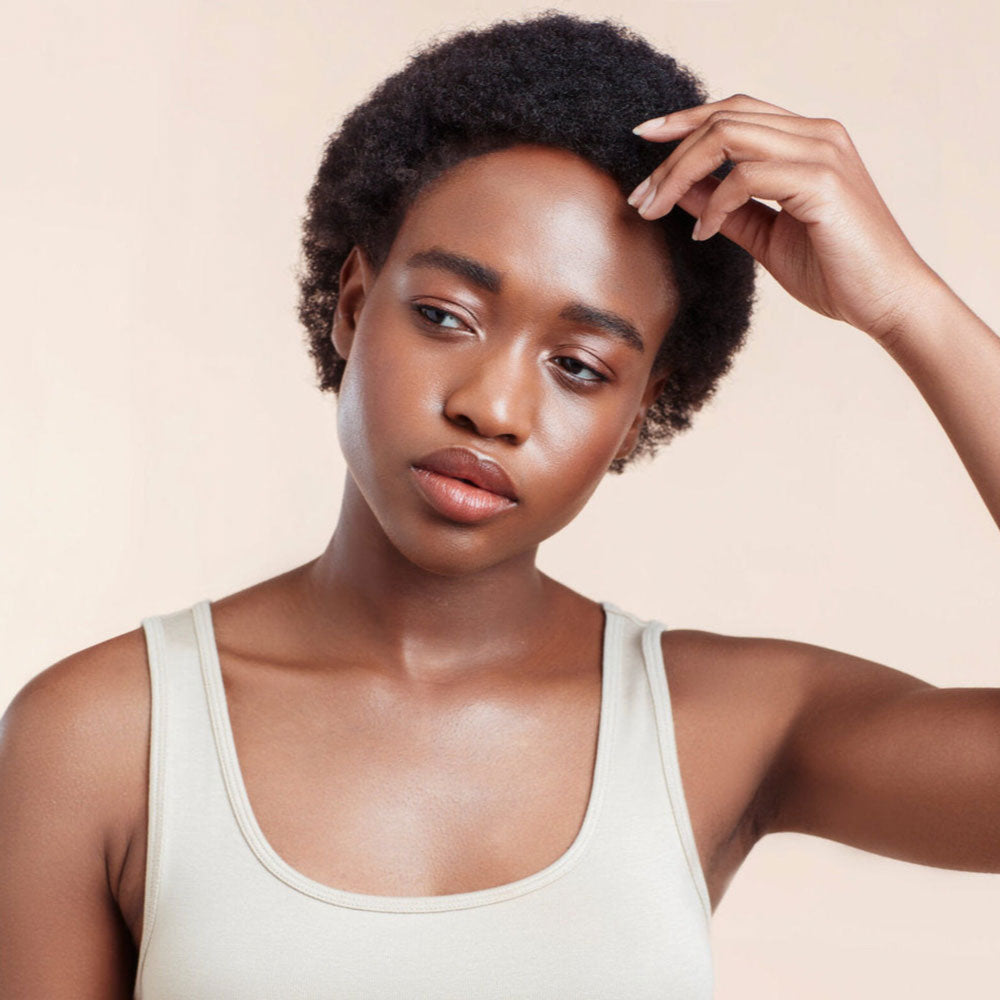 Woman with natural hair wearing a white tank top against a beige background