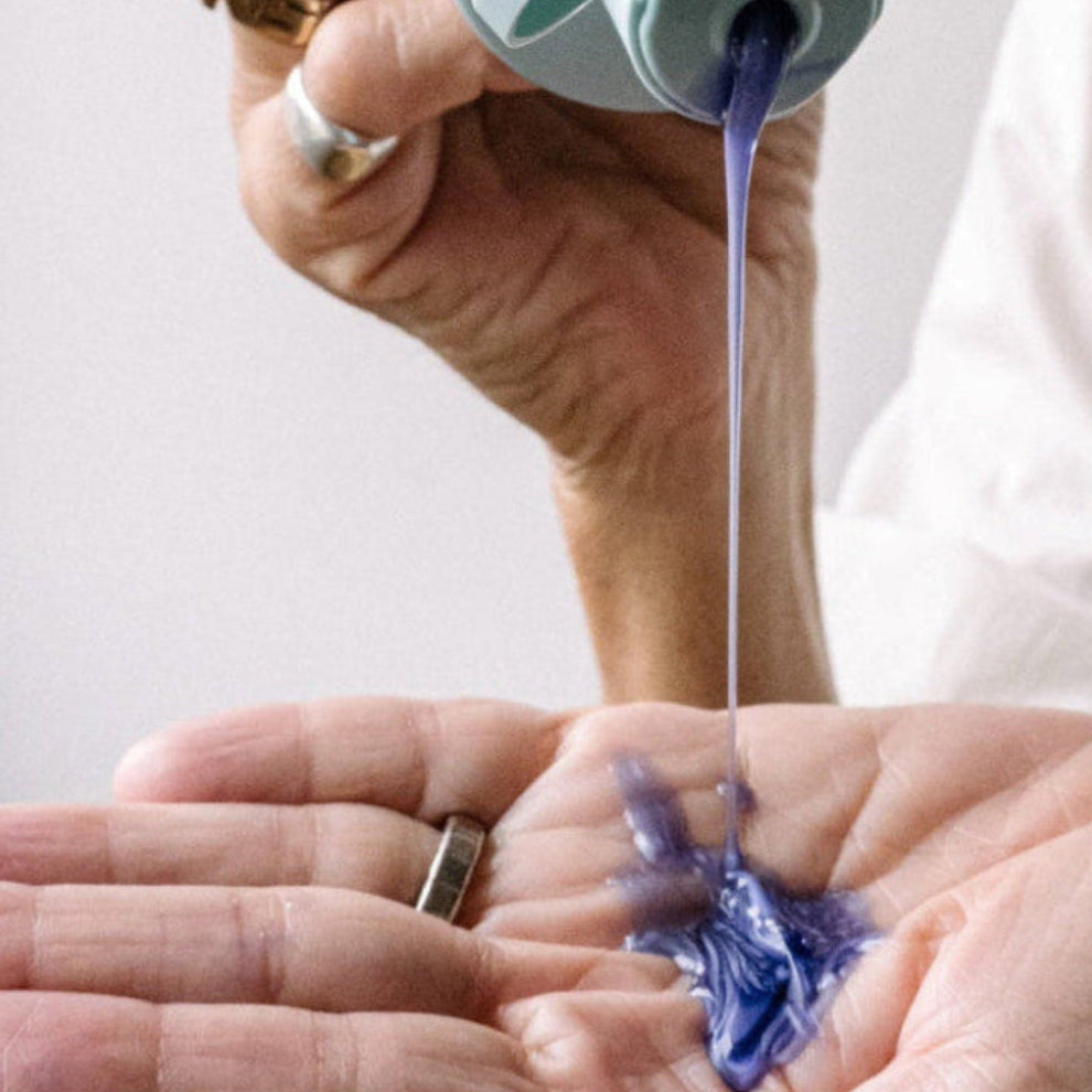 Hand holding a small amount of blue liquid from a bottle against a plain background