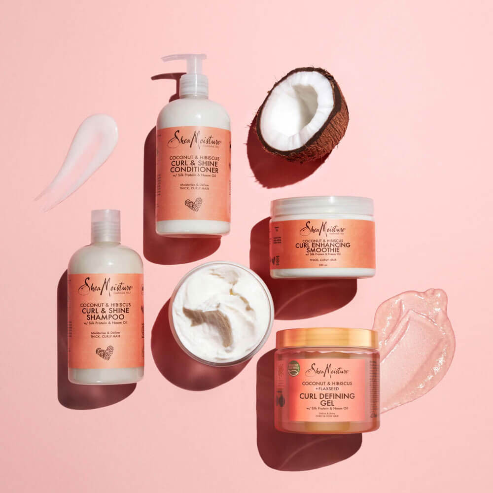 Set of hair care products including shampoo, conditioner, and masks on a pink background with a coconut half.