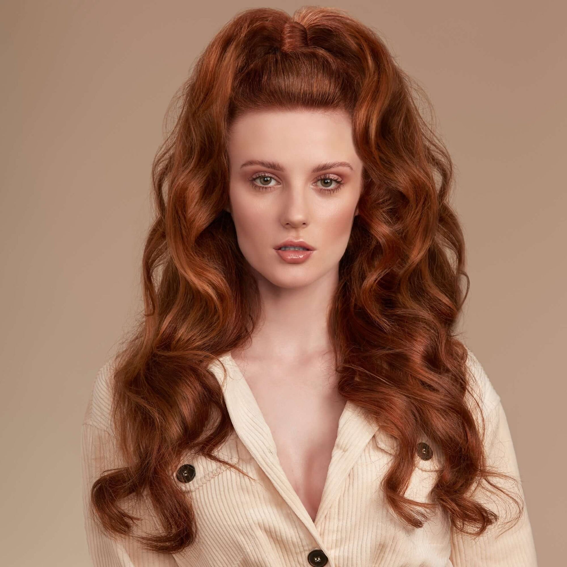 Woman with long, wavy red hair wearing a light-colored blouse against a beige background
