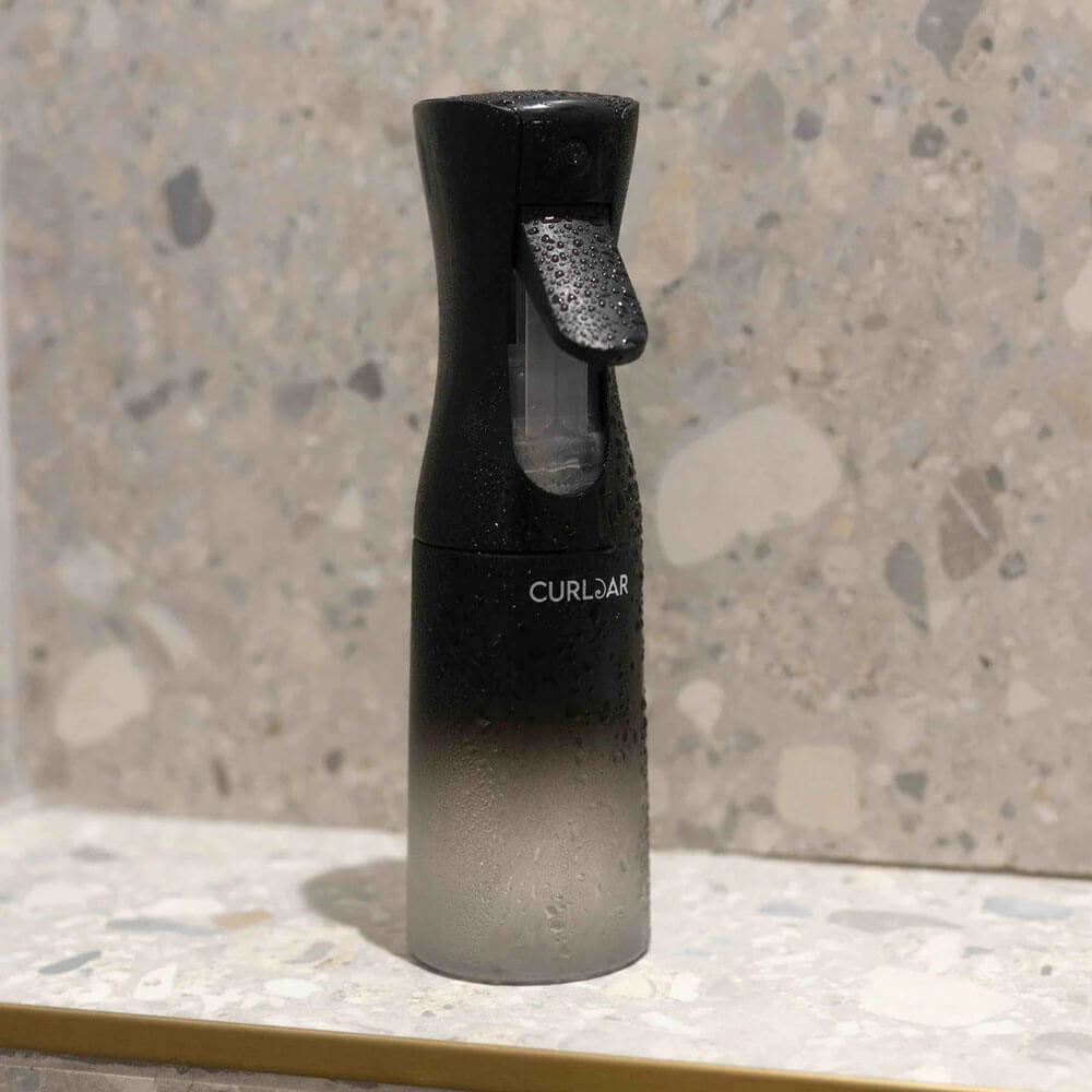 Black and clear spray bottle labeled 'CurlJar' on a textured surface
